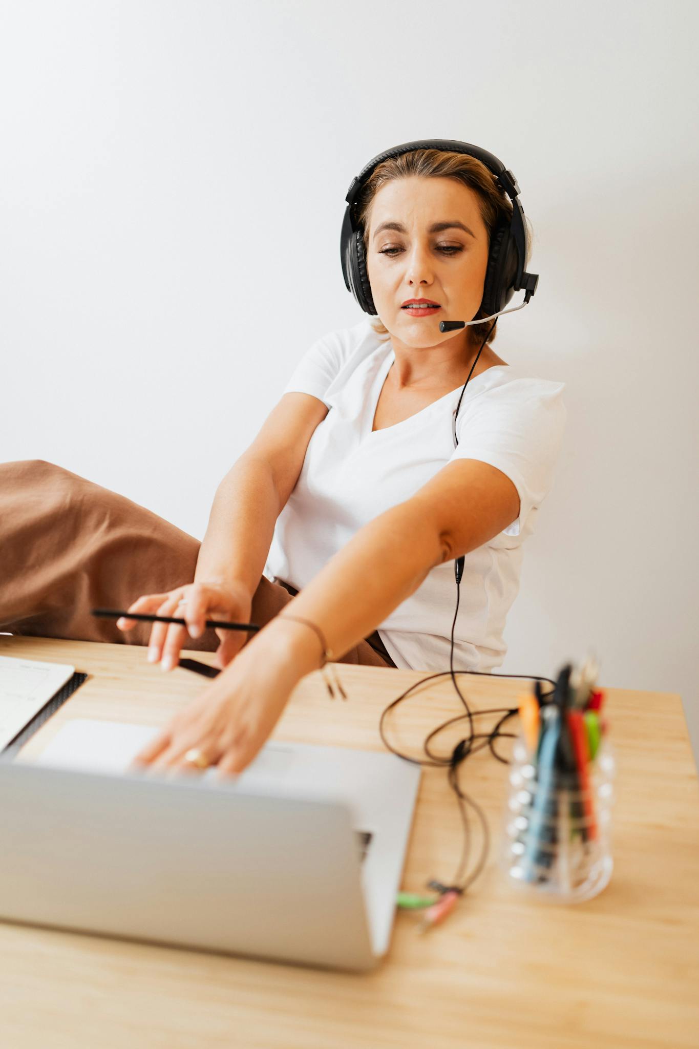 Focused woman in a call center setting working on a laptop with a headset and microphone.